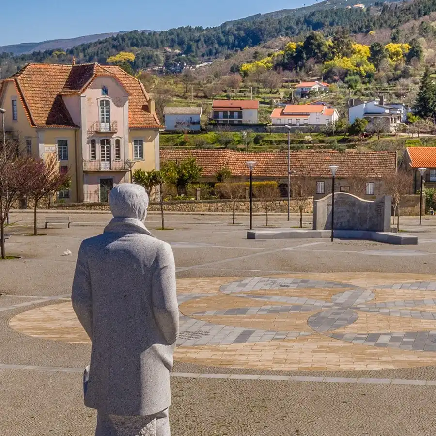 Pueblo serrano con estatua, arquitectura tradicional y vistas montañosas.