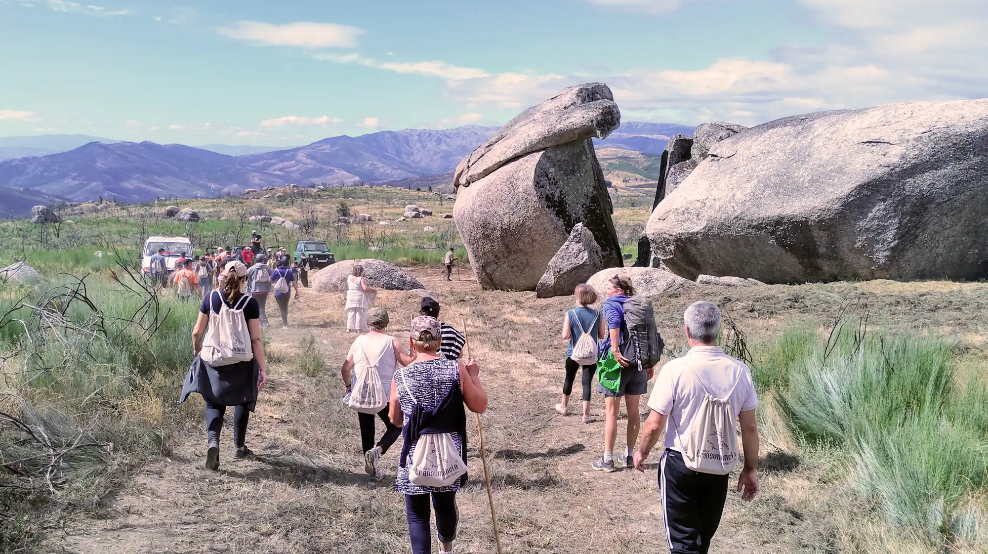 Hiker walking along a granite trail in Serra da Estrela with mountain views in the background.