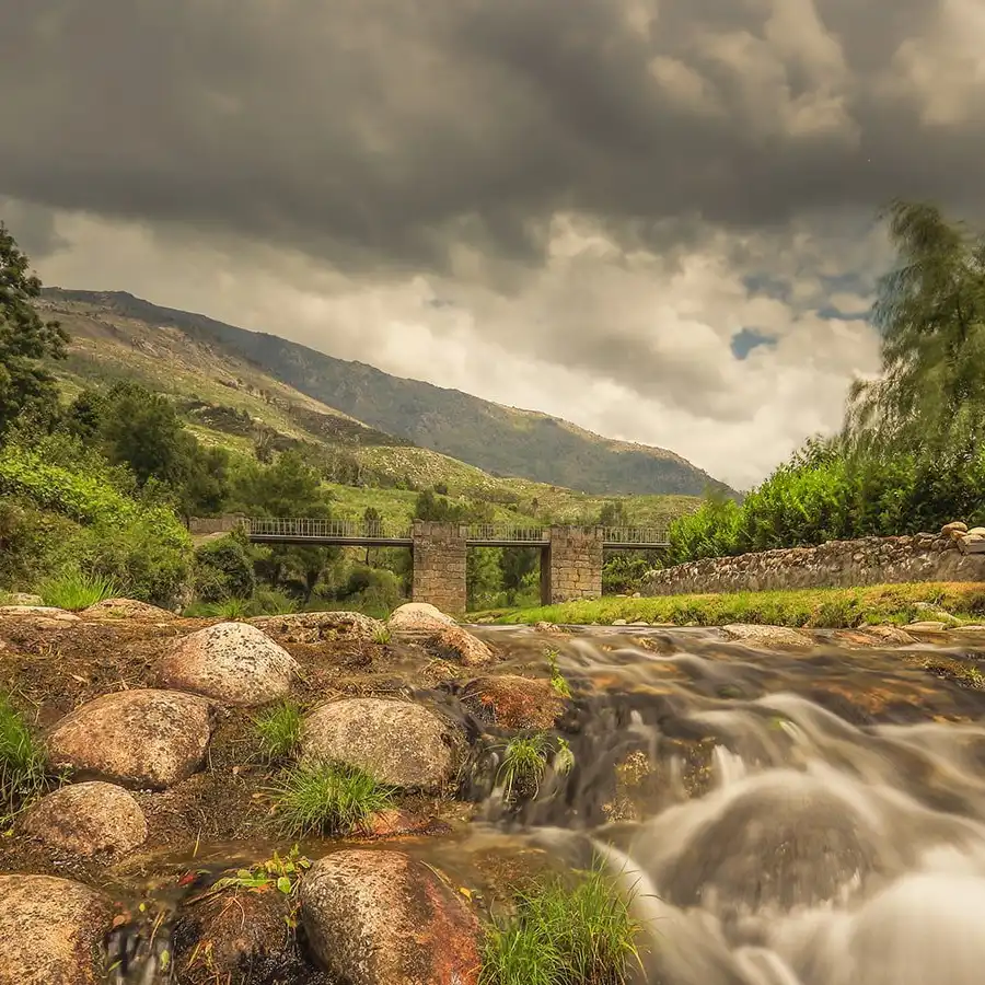 Paisagem serena na Serra da Estrela: rio, ponte e a beleza da natureza.