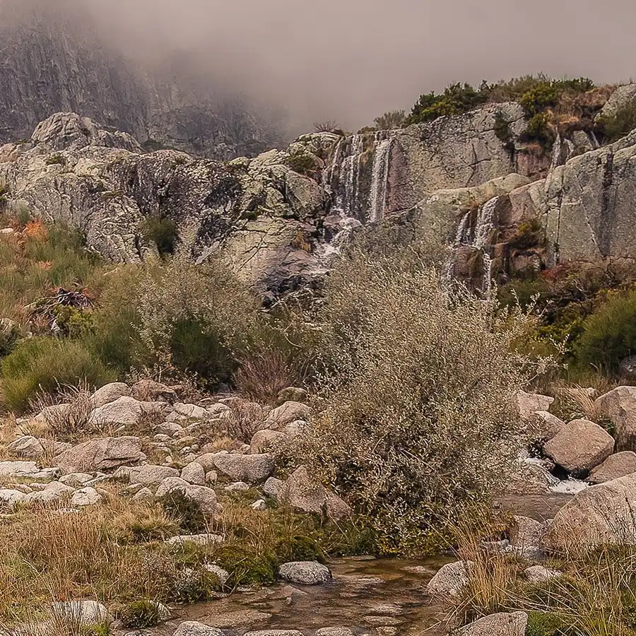 Paisagem serena da Serra da Estrela: rochas, vegetação e um ribeiro cristalino.