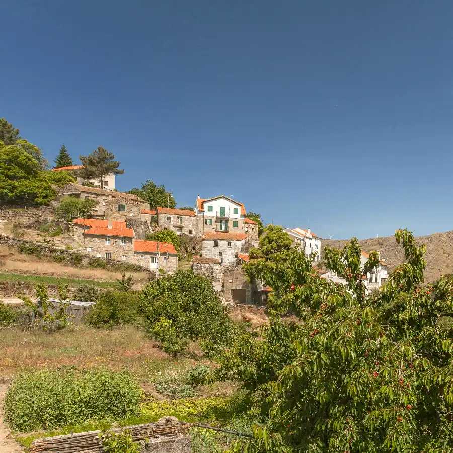 Paisagem rural tranquila com casas tradicionais e plantações na Serra da Estrela.
